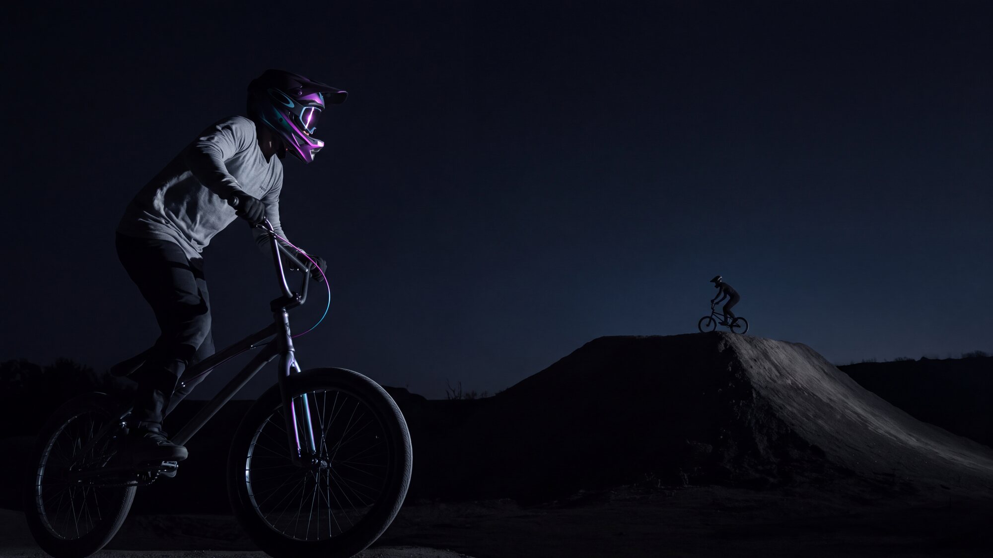 Illustrazione: la silhouette di un ciclista BMX in controluce sul colmo di un dosso, minuscola dentro un’inquadratura molto larga e buia