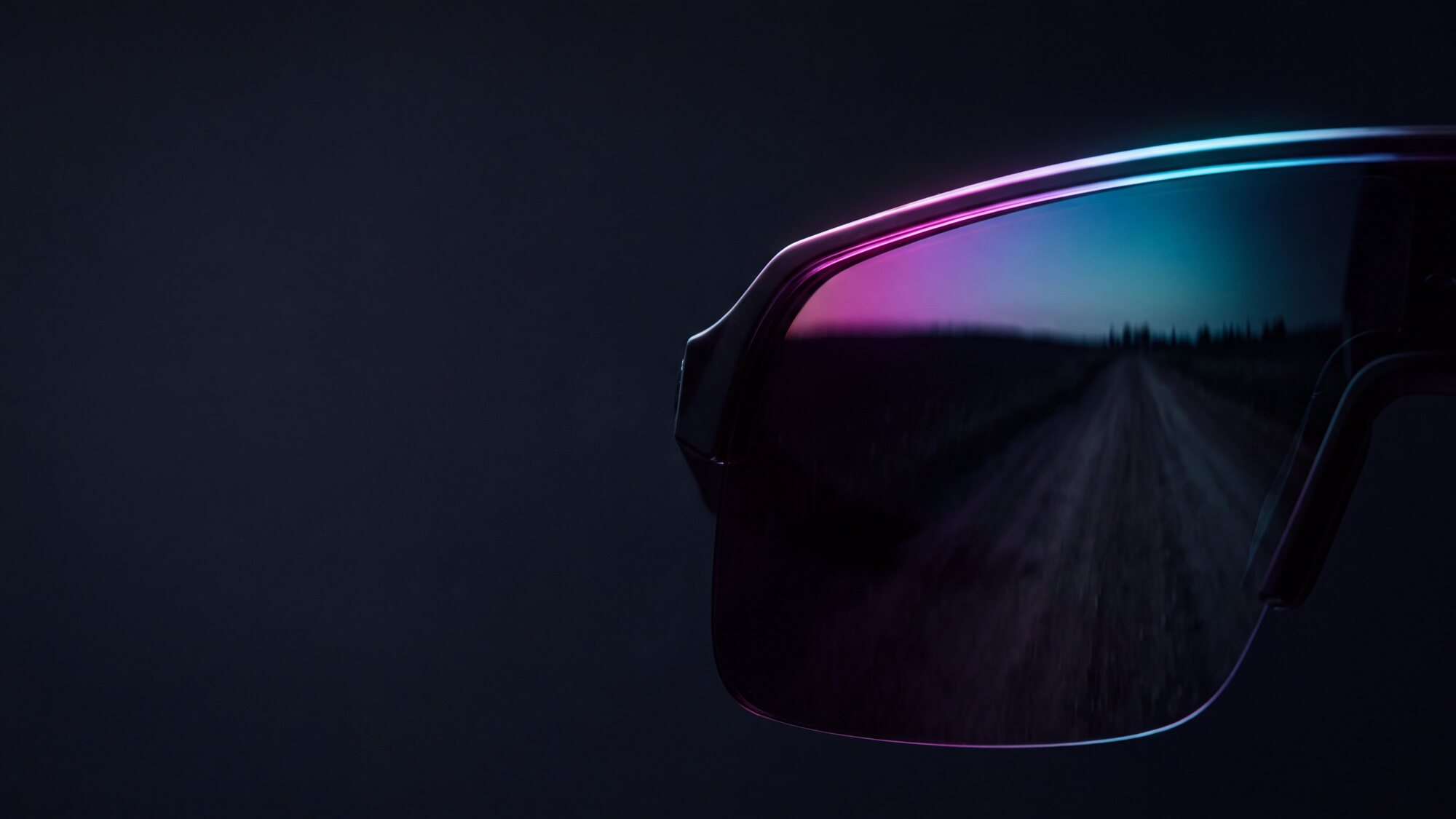 Illustrazione: primissimo piano di una lente specchiata da occhiale sportivo, ripresa al buio, con il bordo superiore acceso da un riflesso iridescente magenta e ciano